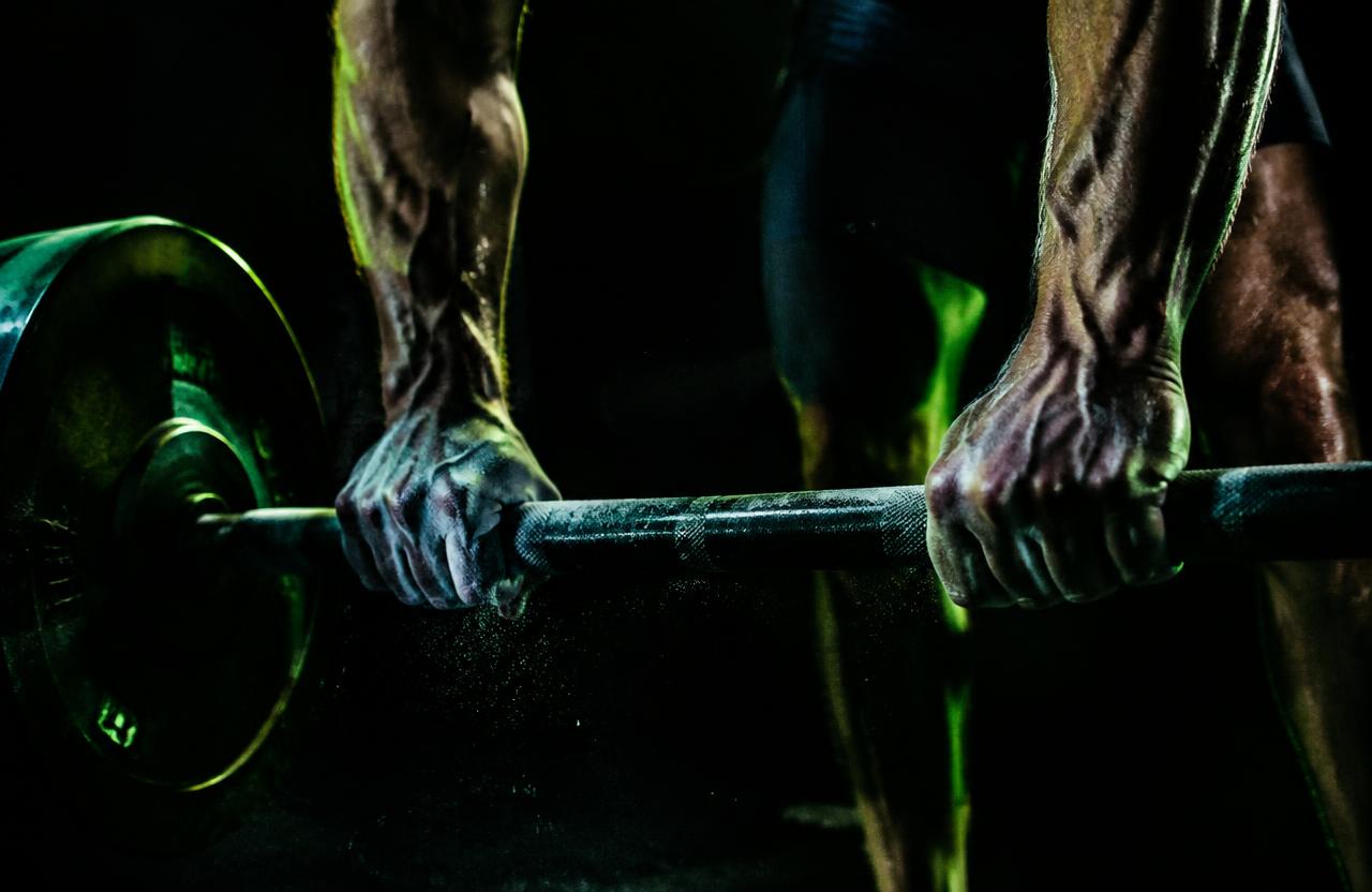 Mãos segurando uma barra de treino em ambiente escuro